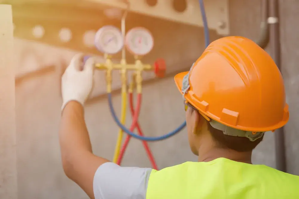 Técnico con casco usando manómetros para revisar un sistema de enfriamiento